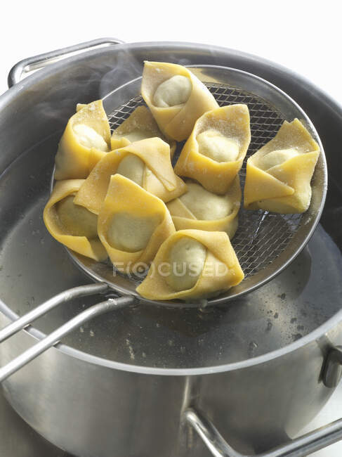 Tortellini fresco en un tamiz con una sartén de agua hirviendo - foto de stock