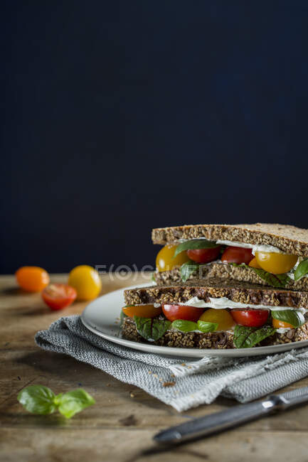 Sandwiches integrales de pan con queso crema, tomates cherry y albahaca - foto de stock