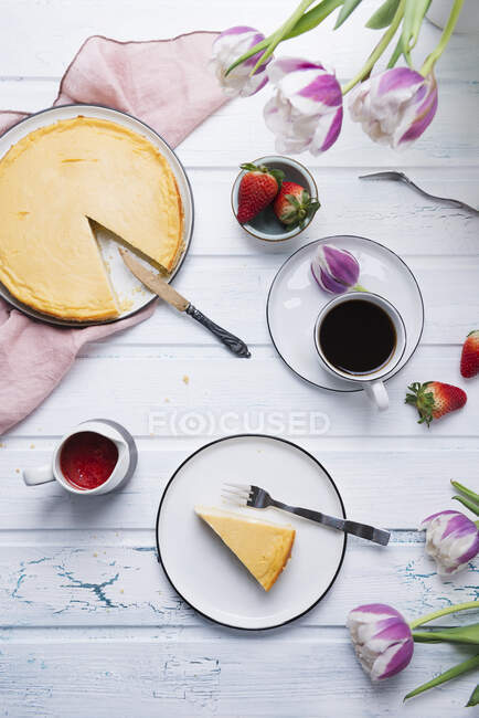 Café servido con pastel de queso vegano, frutas frescas, salsa de fresas y tulipanes - foto de stock