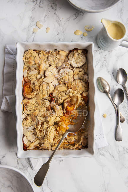 Apricots and almonds crumble pie in tin with spoons on counter — Stock Photo
