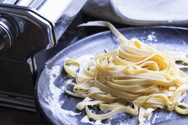 Hausgemachte Pasta auf einem Teller vor einer Nudelmaschine — Stockfoto