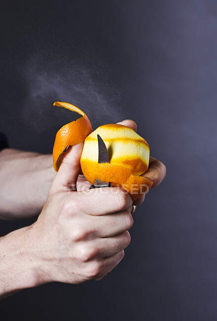 Mãos Descascamento de laranja com faca, suco de pulverização visível — Fotografia de Stock