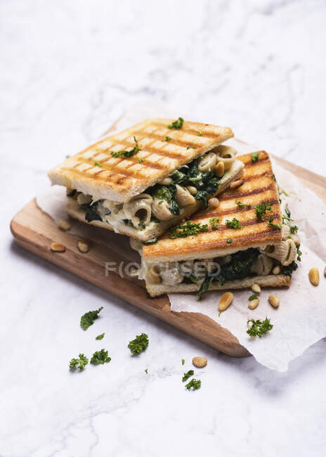 Un sándwich tostado con macarrones veganos y queso, espinacas y piñones - foto de stock