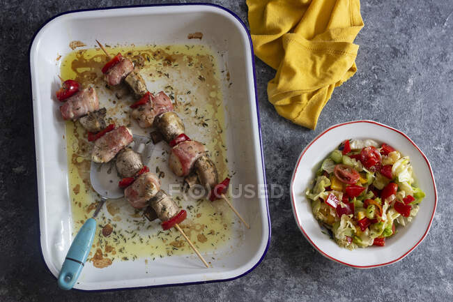 Espetos com frango em bacon, cogumelos e pimenta vermelha, salada de alface, tomate, pimentão, pepino — Fotografia de Stock