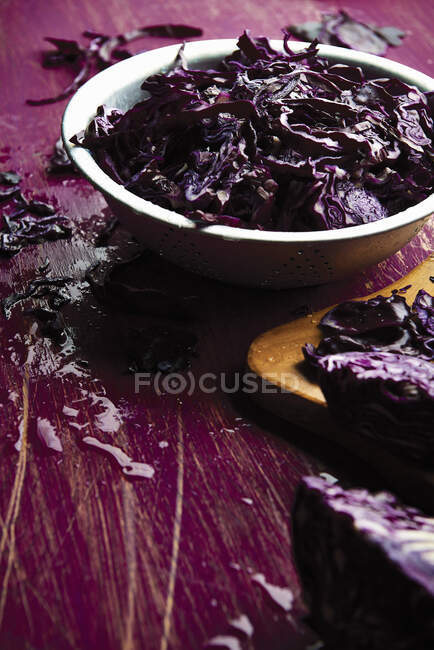 Repolho roxo fatiado em uma tigela com alguns espalhados na mesa — Fotografia de Stock