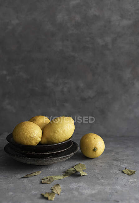 Organic lemons on stacked plates and on concrete surface with dry leaves — Stock Photo
