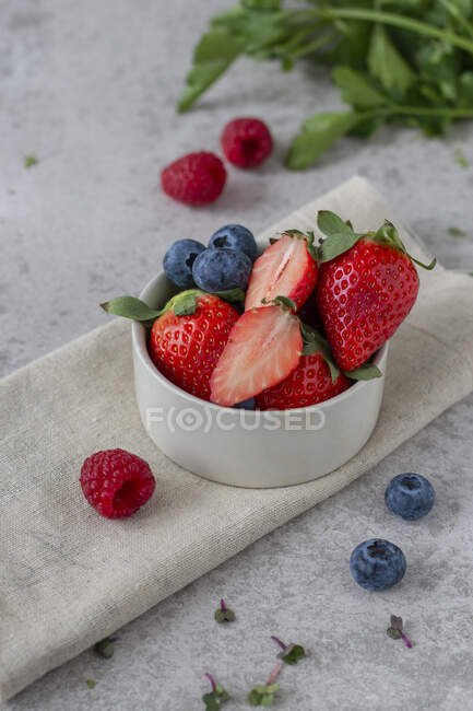 Strawberries, blueberries and raspberries in small bowl and on table — Stock Photo