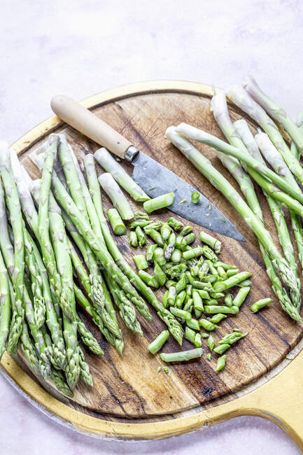 Whole and chopped asparagus with knife on wooden board — Stock Photo