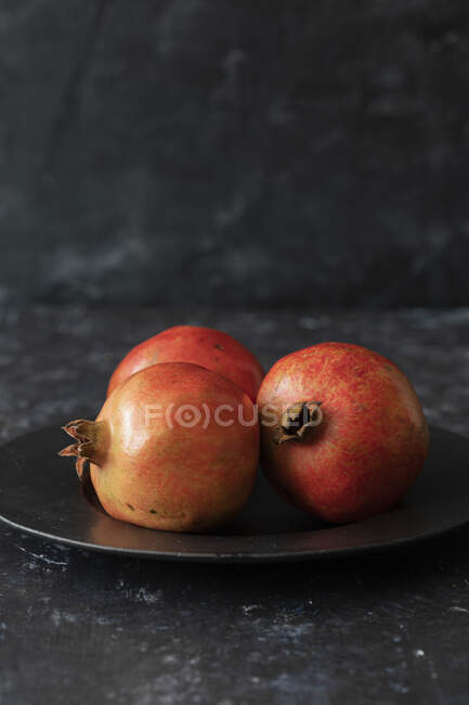 Three Pomegranates in plate on dark background — Stock Photo