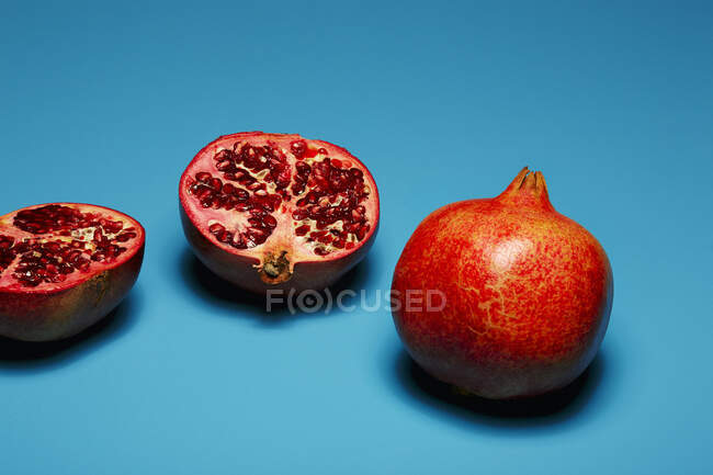 Ganze und halbierte Granatäpfel auf sattblauem Hintergrund — Stockfoto