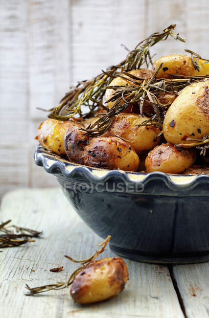 Roasted potatoes with sprigs of rosemary in ceramic bowl — Stock Photo