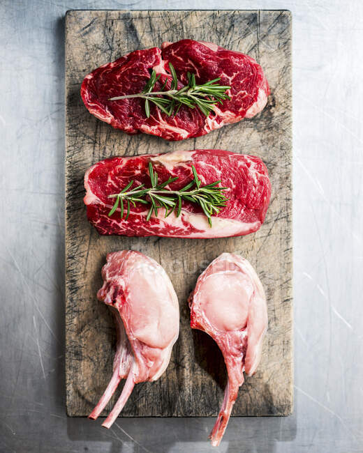 Viande crue steak de boeuf au romarin et thym sur une planche de bois — Photo de stock