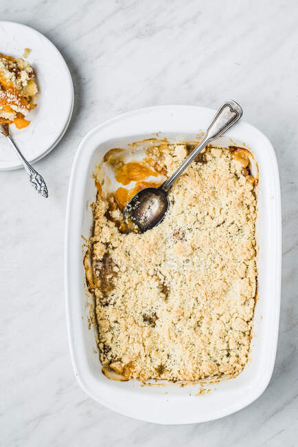 Crumble pie with apricots, cardamon, ginger and cinnamon in tin and piece on plate — Stock Photo