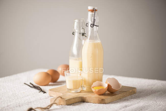 Eggnog in bottles and glass with cracked egg on wooden board — Stock Photo