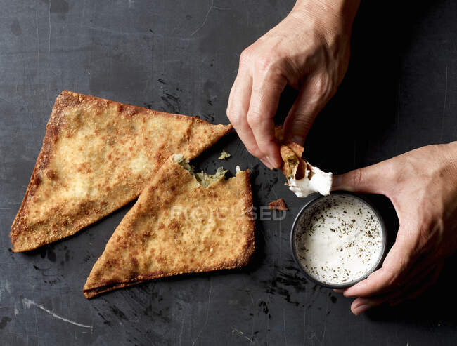 Hände tauchen Bolani-Brot in Joghurtsoße — Stockfoto