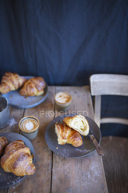 Croissants with cappuccinos on a rustic wooden table — Stock Photo