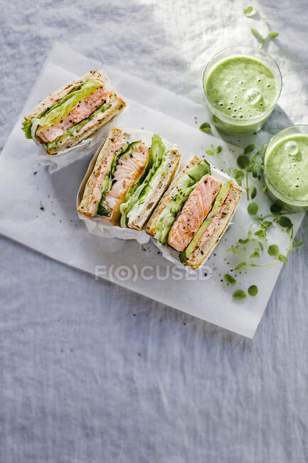 Sandwich de tostadas con salmón, pepino, aguacate, caviar y queso cremoso, servido con smoothy verde - foto de stock
