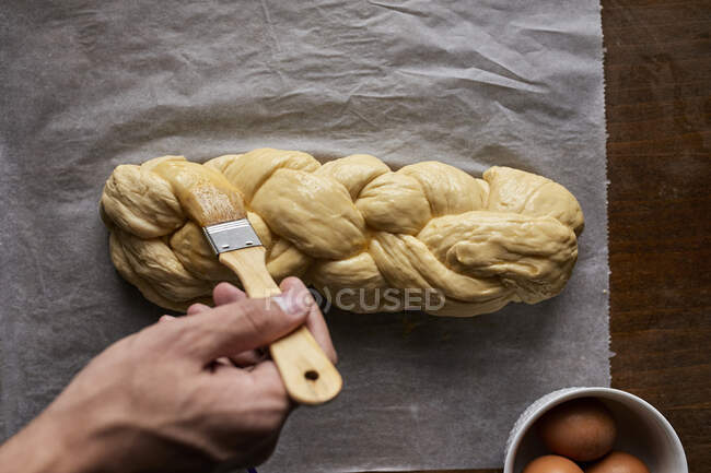 Um pão trançado sendo espalhado com gema de ovo — Fotografia de Stock