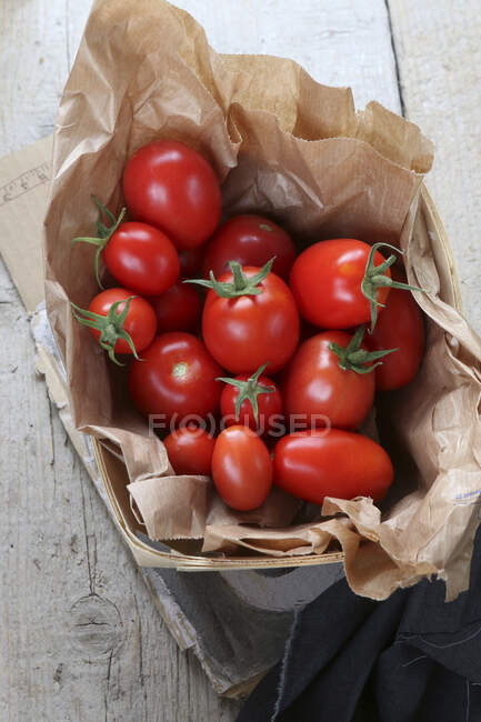 Tomates fraîches de vigne dans un sac en papier dans un panier en bois — Photo de stock