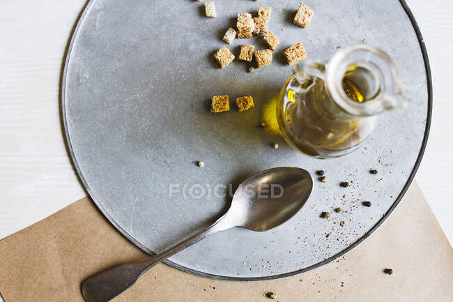 A small carafe of olive oil, croutons, a spoon and pepper on a plate — Stock Photo
