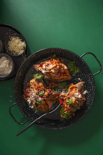 Chipotle bean chilli with baked sweet potatoes, grated cheese, coriander and sour cream — Stock Photo