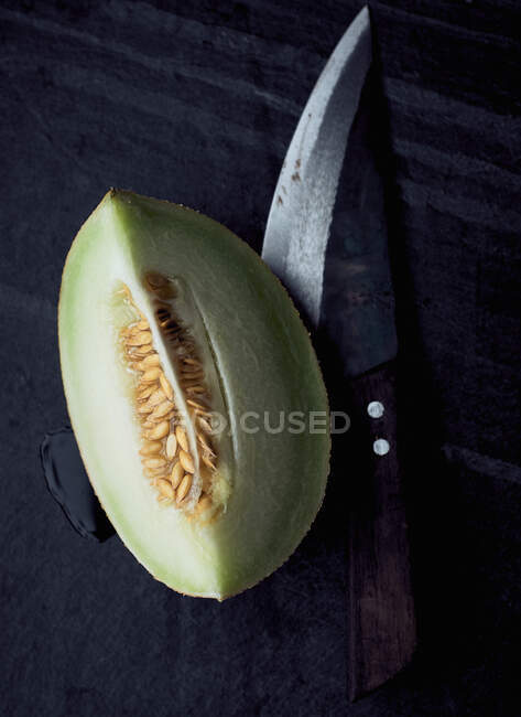 Cuneo di melone su superficie in pietra nera con coltello rustico — Foto stock
