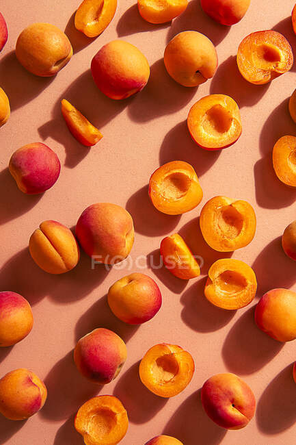 Aprikosen, ganz und halbiert auf rosa Hintergrund im Sonnenlicht — Stockfoto