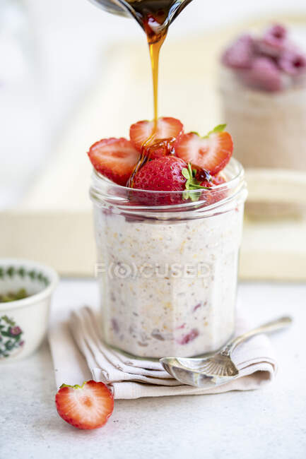 Overnight oats with strawberries and dripping syrup from glass jug — Stock Photo