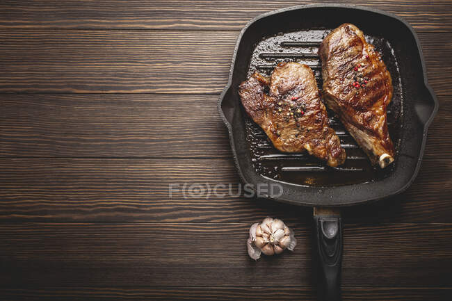 Due bistecche bruciate in una padella su una superficie di legno — Foto stock
