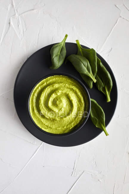 Hummus di spinaci in ciotola con foglie sul piatto — Foto stock