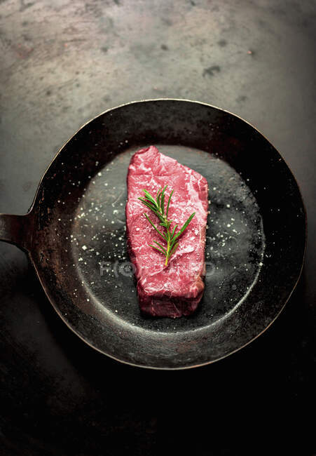 Una bistecca di manzo con rosmarino in una padella — Foto stock