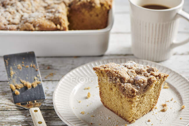 A piece of crumb cake served on a white plate with a white coffee mug filled with coffee — Stock Photo