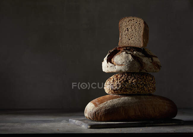 Quatre pains différents, empilés sur fond sombre — Photo de stock