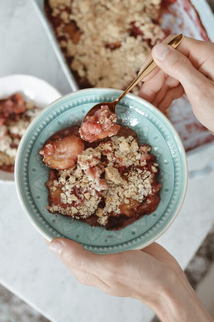 Hands holding bowl of baked plums with crumbles — Stock Photo