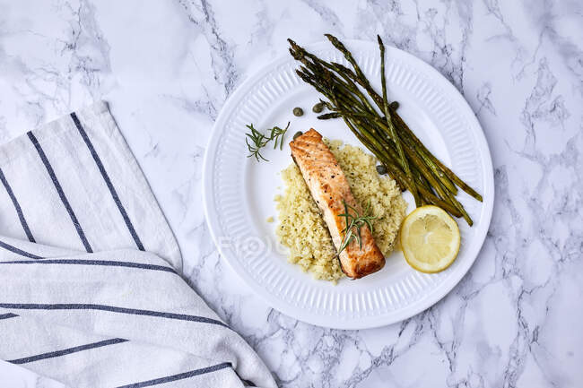 Baked salmon served on couscous with asparagus and caper on the side — Stock Photo