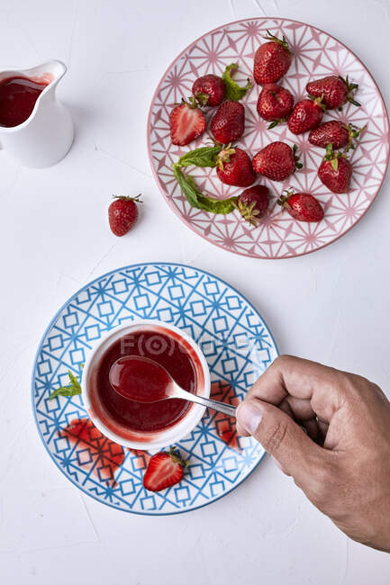 Hand holding spoon of Homemade strawberry sauce and fresh strawberries on plate — Stock Photo