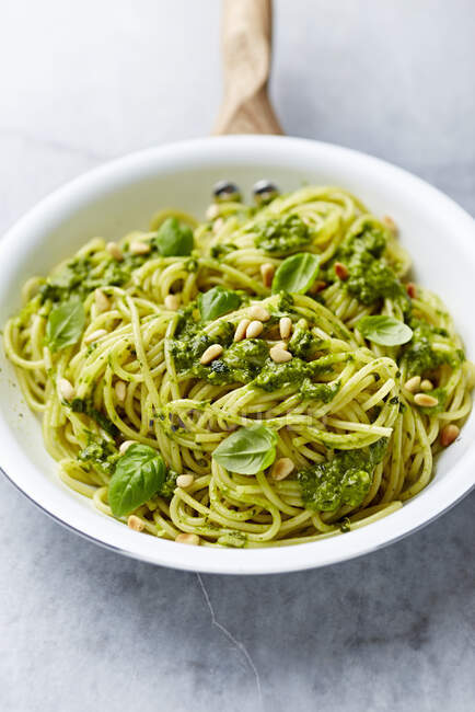 Spaghetti with spinach pesto, toasted pine nuts and basil leaves in a pan — Stock Photo
