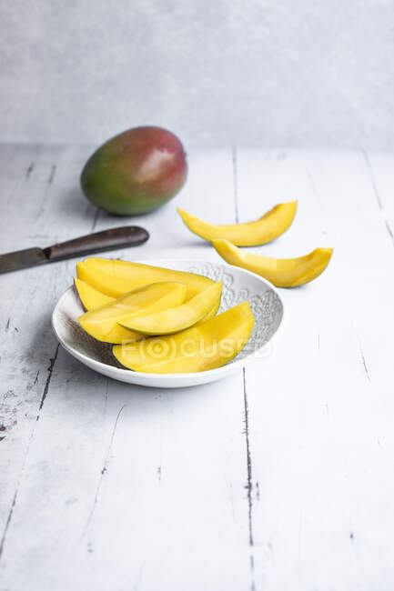 Fette intere di mango e mango in piatto e sul tavolo con coltello — Foto stock