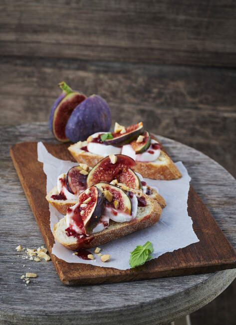 Baguette topped with figs and goat's cream cheese on wooden board — Stock Photo