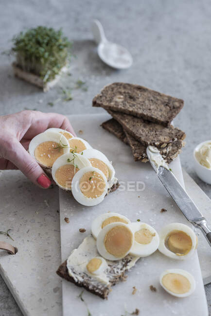 Mano sosteniendo rebanada de pan rematada con huevos duros - foto de stock