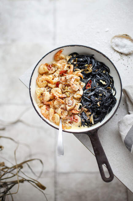 Креветки в карамельном луке и сливочном соусе с черными спагетти — стоковое фото