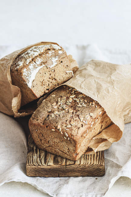 Two loaves of rye bread in paper bags on wooden board — Stock Photo
