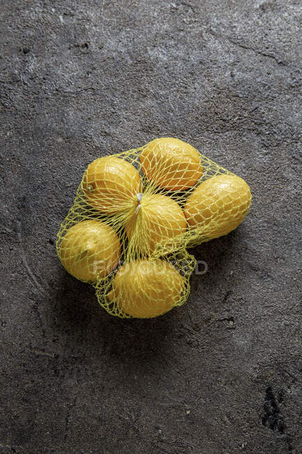 Limões em saco de grade na superfície de pedra — Fotografia de Stock