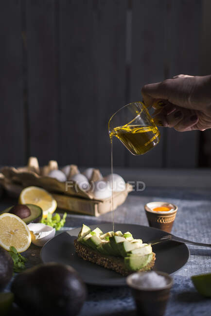 Olive oil being poured from a glass jug onto avocado bread — Stock Photo