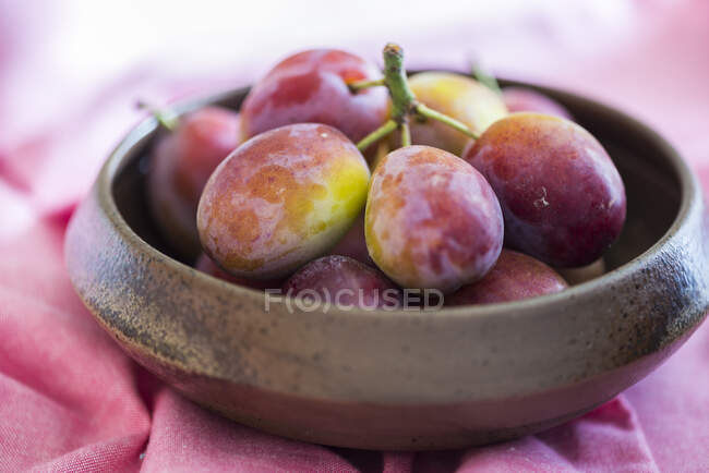 Prugne fresche in ciotola di legno su panno rosa — Foto stock