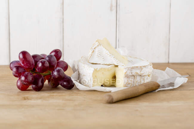 Camembert cheese with knife and fresh red grapes — Stock Photo