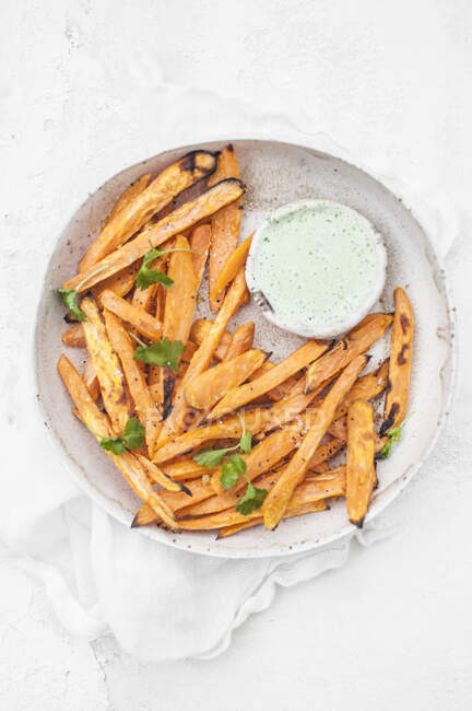 Sweet potatoes fries served with jalapeno yoghurt sauce and fresh cilantro — Stock Photo