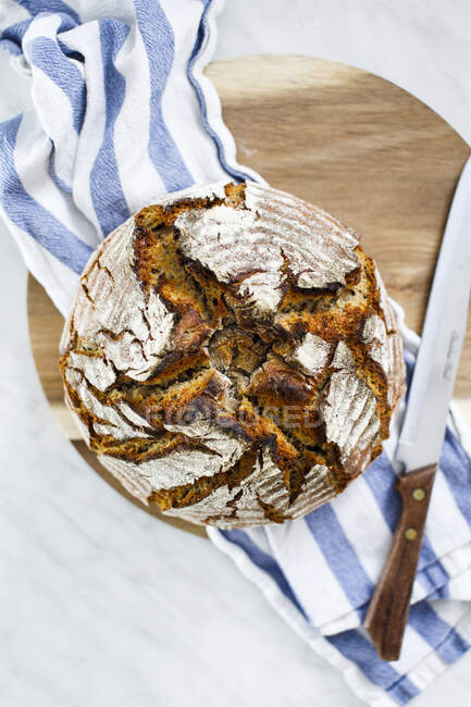 Sourdough rye bread on wooden board with cloth and knife — Stock Photo