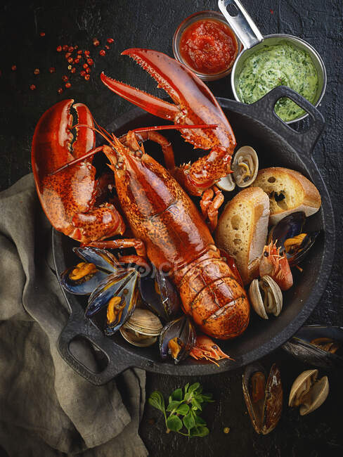 Cooked lobster, mussels and prawns with bread in pot — Stock Photo