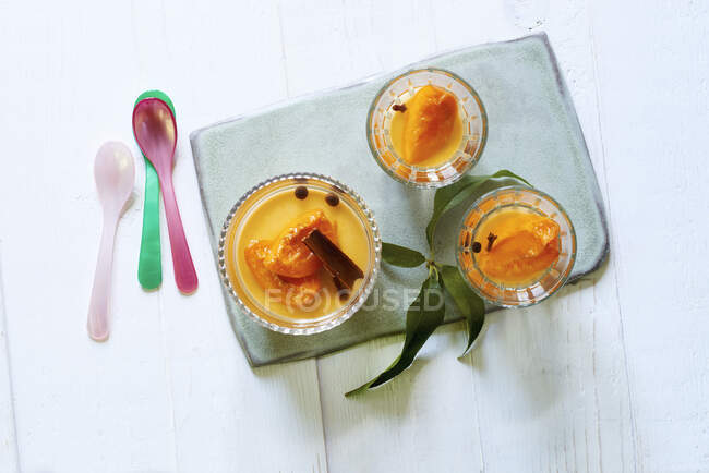 Charred honey panna cotta with apricots in glasses and green leaves on stone board — Stock Photo